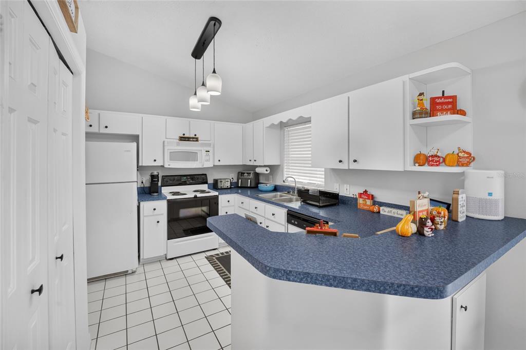 A kitchen features white cabinets, blue laminate countertops, white appliances, and white tile flooring — 11625 SE 53RD COURT, BELLEVIEW, FL