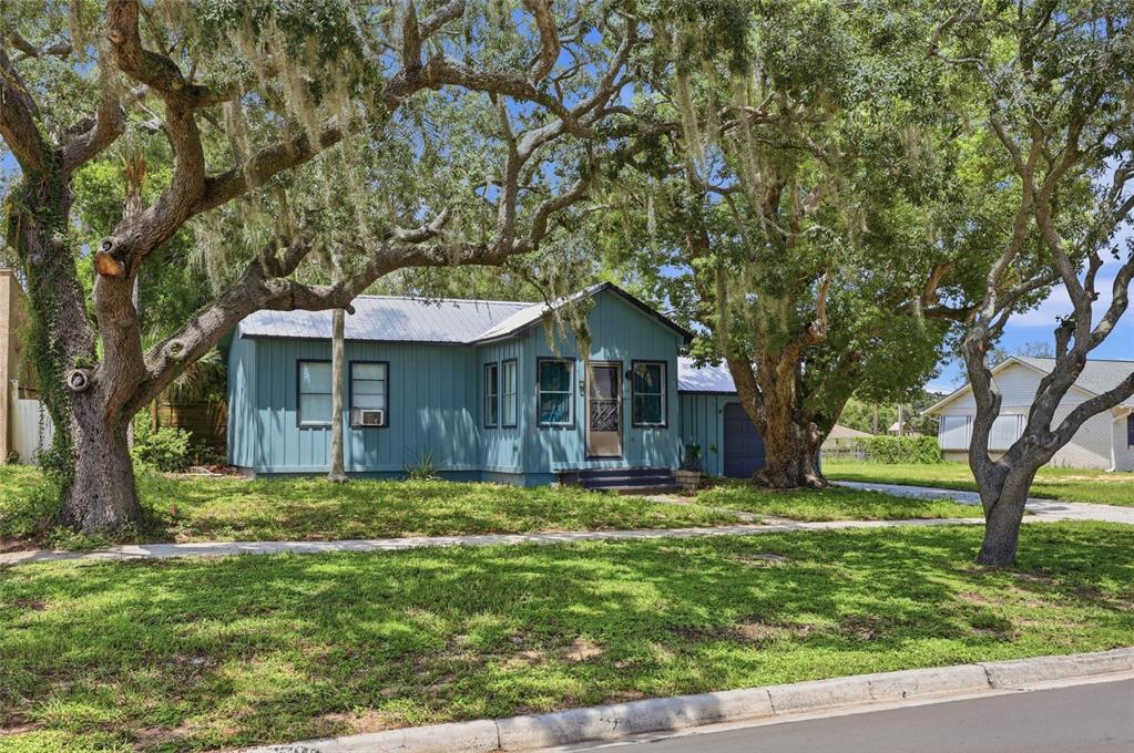 A blue single-story house with a metal roof sits under large oak trees — 4 E BAY STREET, DAVENPORT, FL