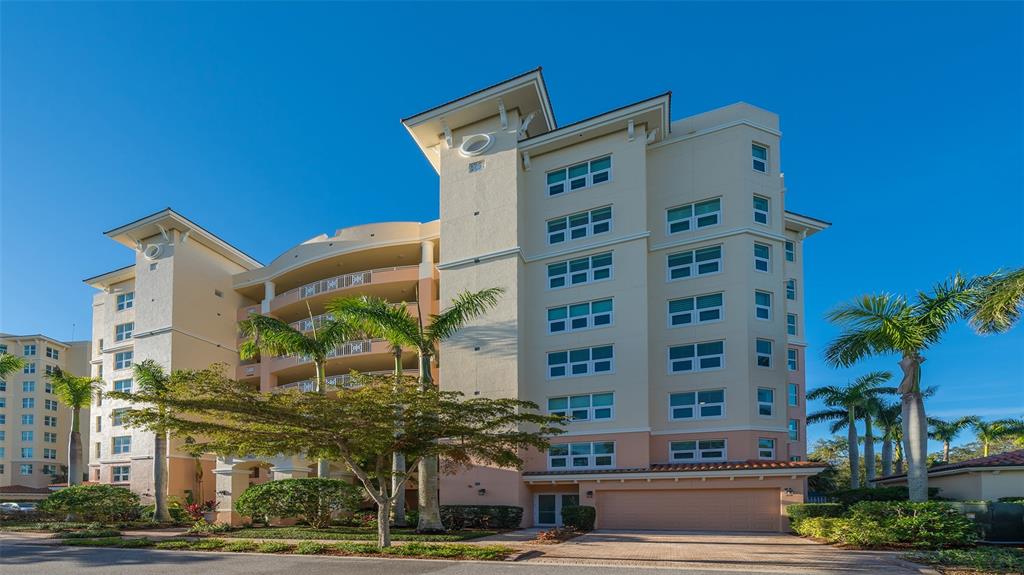 A multi-story beige apartment building features balconies, palm trees, and a ground-level garage — 3621 N POINT ROAD UNIT 301, OSPREY, FL