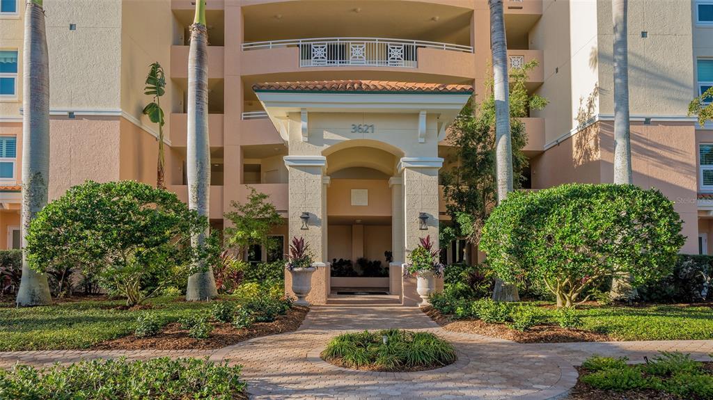 The exterior entrance of a multi-story apartment building features a covered walkway and palm trees — 3621 N POINT ROAD UNIT 301, OSPREY, FL