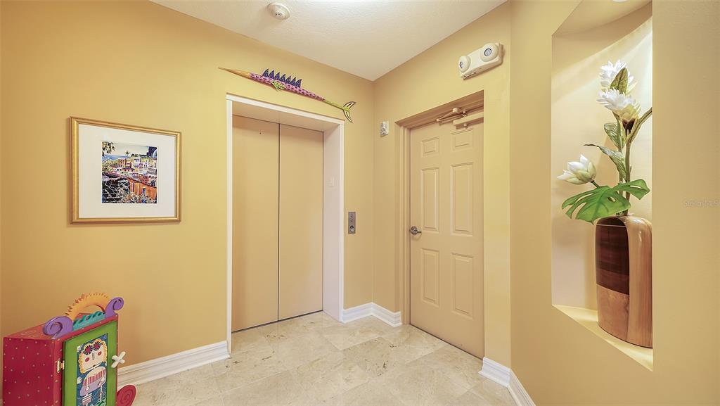 A foyer with a beige elevator, a closed door, and a decorative wall niche with flowers — 3621 N POINT ROAD UNIT 301, OSPREY, FL
