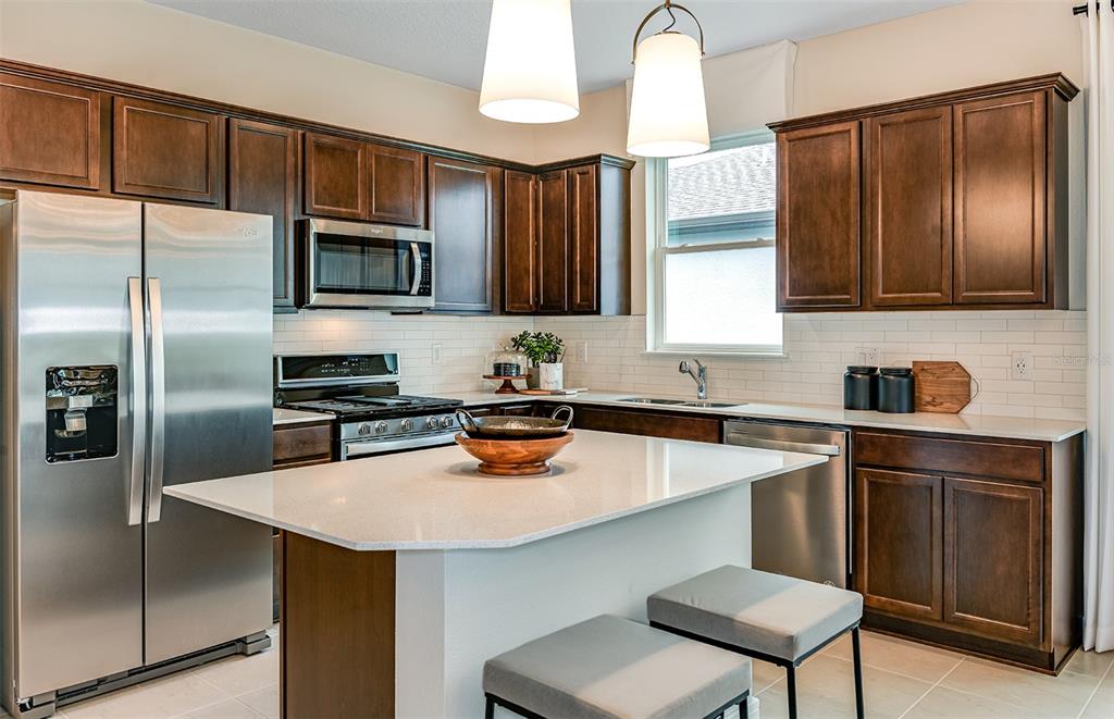 A kitchen with dark wood cabinets, stainless steel appliances, a white island, and pendant lighting — 12510 ADOBE STREET, PARRISH, FL