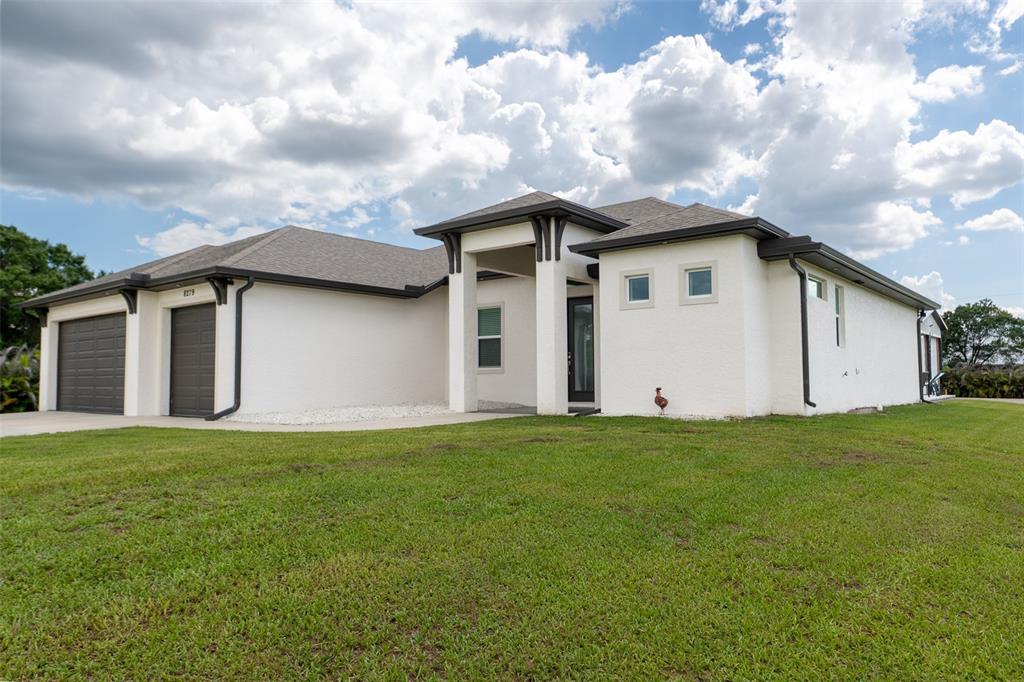 A single-story white stucco house features a dark-trimmed entryway and a two-car garage — 8279 ALFRED BOULEVARD, PUNTA GORDA, FL