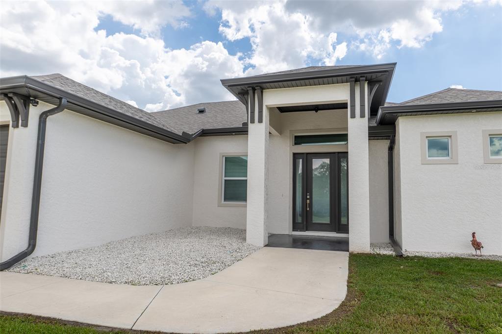 A modern single-story house exterior features a covered entryway, white stucco walls, and dark trim — 8279 ALFRED BOULEVARD, PUNTA GORDA, FL