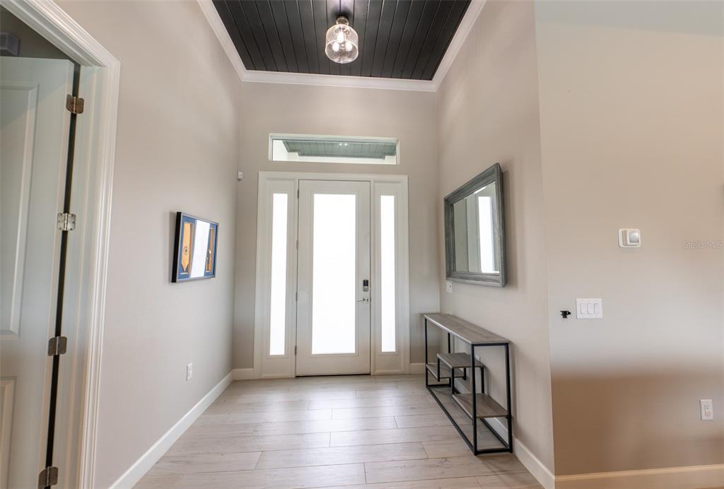 A bright entryway features light wood-look tile flooring, a dark wood ceiling, and a glass-paneled door — 8279 ALFRED BOULEVARD, PUNTA GORDA, FL