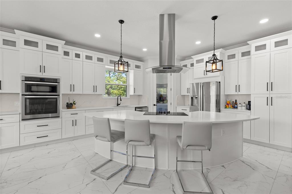 A modern white kitchen features a large curved island, stainless steel appliances, and marble-look flooring — 1924 HILL DRIVE, APOPKA, FL