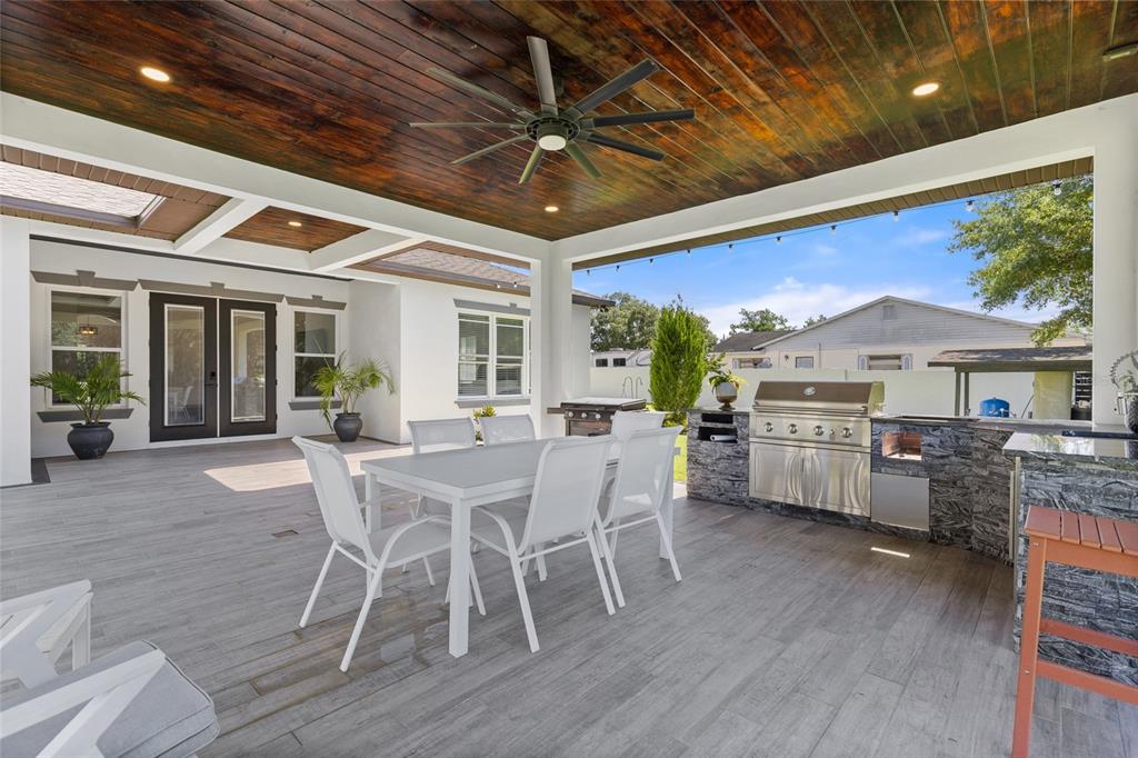 A covered outdoor patio features a dining set, a built-in grill, and wood-paneled ceilings — 1924 HILL DRIVE, APOPKA, FL
