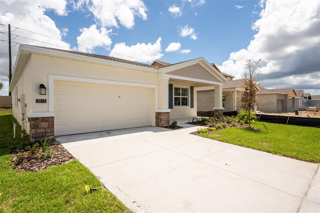 A single-story suburban house features a two-car garage, stone accents, and a covered entryway — 2015 PUNCH BOWL AVENUE, DAVENPORT, FL
