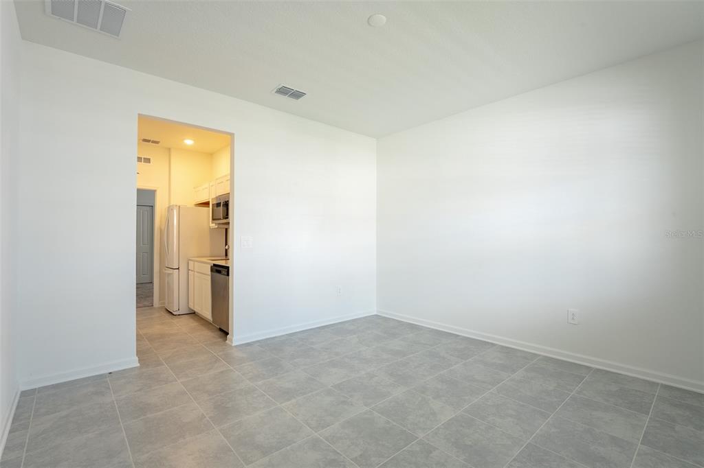 A room with light gray tile flooring and white walls leads into a small kitchen — 2015 PUNCH BOWL AVENUE, DAVENPORT, FL