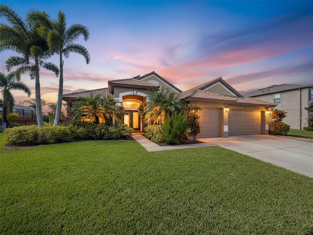 A single-story house with a tile roof, three-car garage, and palm trees at sunset — 335 COCKLE SHELL LOOP, APOLLO BEACH, FL