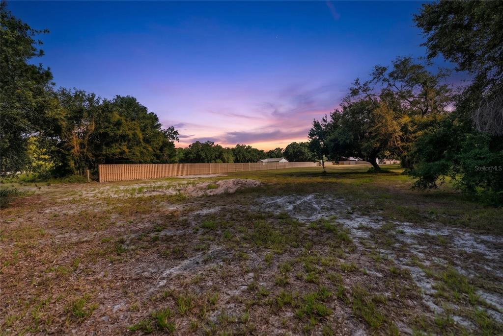A large, grassy, partially cleared lot features scattered trees and a long wooden privacy fence — 15580 COUNTY ROAD 675, PARRISH, FL
