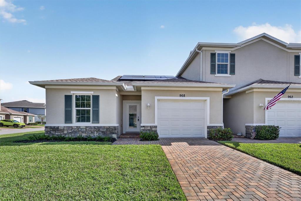 A tan two-story townhouse features a stone-accented facade, a white garage door, and solar panels — 968 NE TRAILSIDE RUN, PORT ST LUCIE, FL