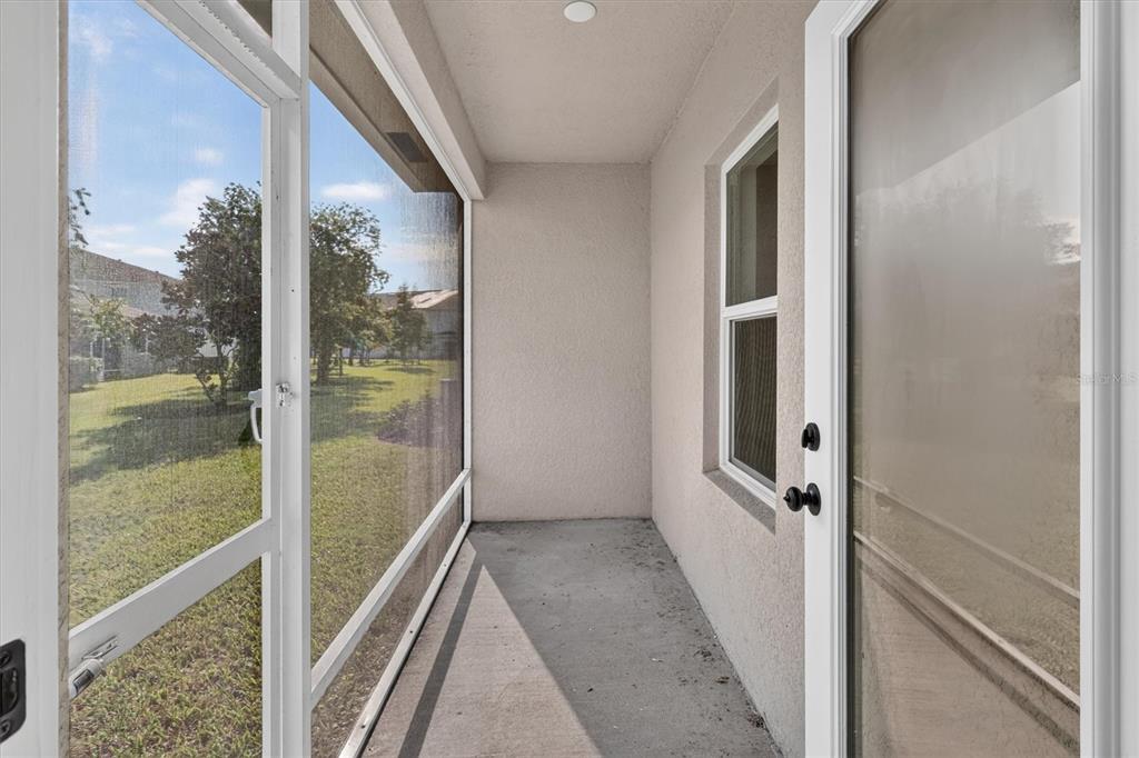 A covered concrete patio features a screened-in wall overlooking a grassy yard — 968 NE TRAILSIDE RUN, PORT ST LUCIE, FL