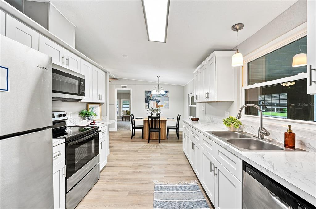 A galley kitchen features white cabinets, marble-look countertops, stainless steel appliances, and light wood flooring — 2055 S FLORAL AVENUE UNIT 117, BARTOW, FL