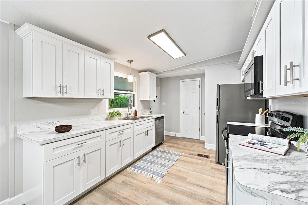 A kitchen features white cabinets, stainless steel appliances, and marble-look countertops with wood-style flooring — 2055 S FLORAL AVENUE UNIT 117, BARTOW, FL