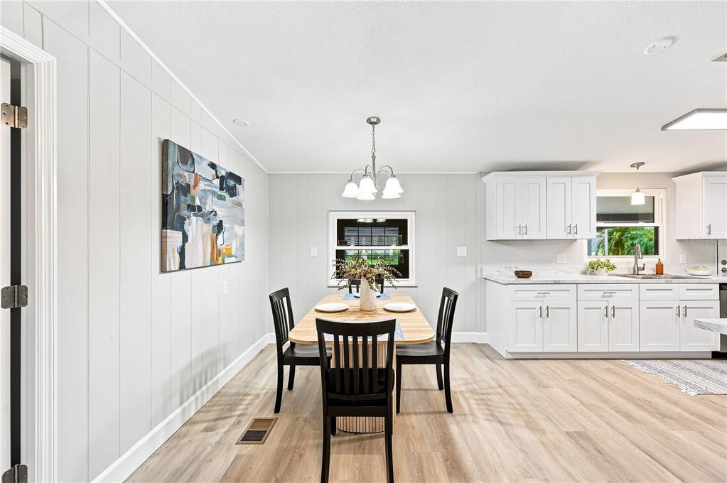 A kitchen with white cabinets, marble-look countertops, and stainless steel appliances leads to a dining area — 2055 S FLORAL AVENUE UNIT 117, BARTOW, FL