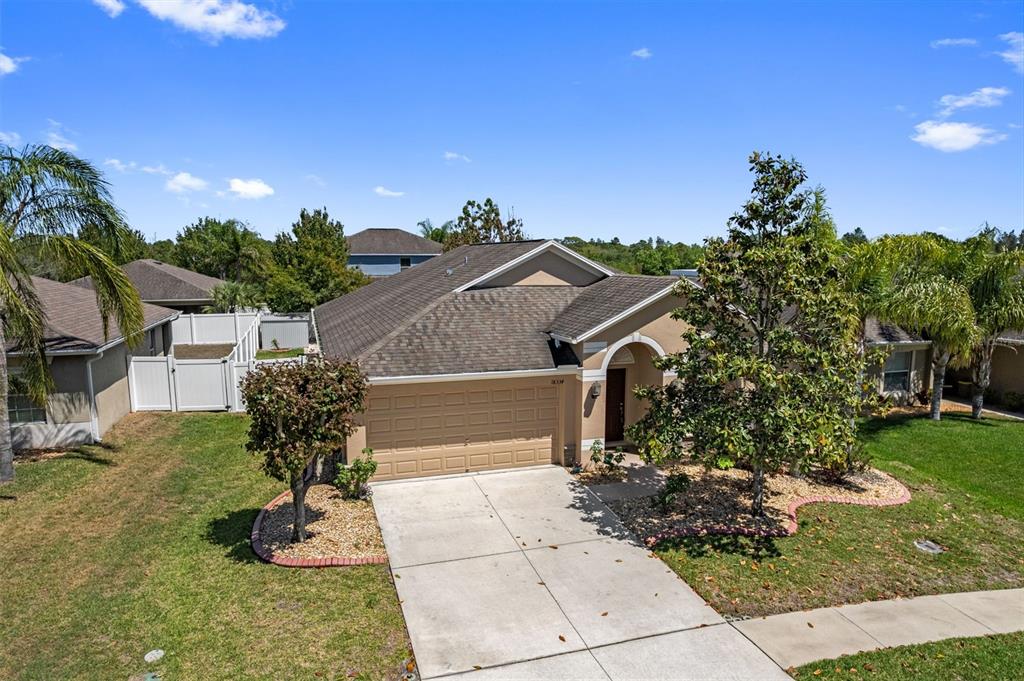 An exterior view of a single-story house with a tan facade, garage, and front yard — 18334 WAYDALE LOOP, HUDSON, FL