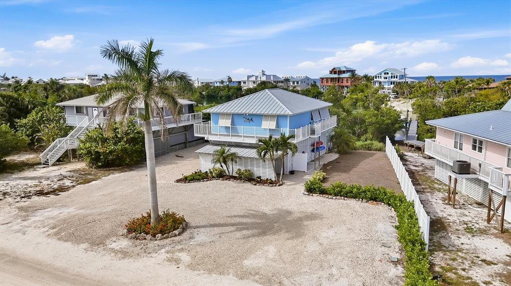 An elevated blue house with a metal roof stands on a gravel lot with palm trees — 21 BOCILLA DRIVE, PLACIDA, FL