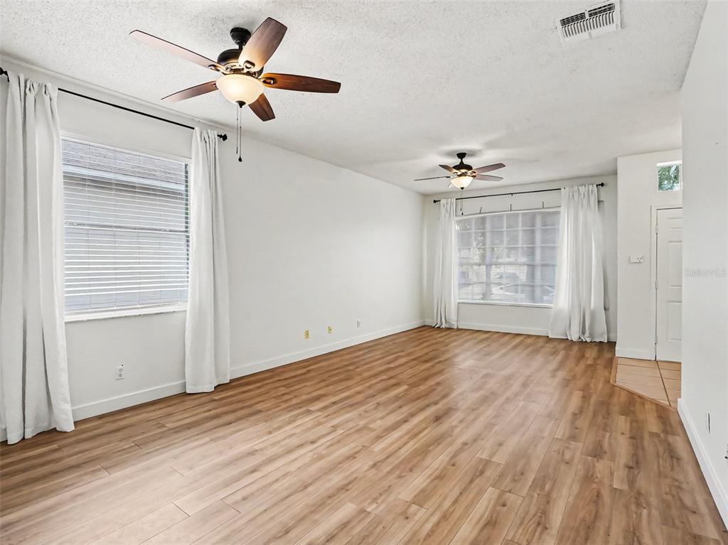 An empty living room features wood-look flooring, white walls, two ceiling fans, and large windows — 14523 KRISTENRIGHT LANE, ORLANDO, FL