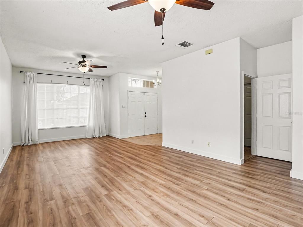 A bright living room features light wood-look flooring, white walls, and two ceiling fans — 14523 KRISTENRIGHT LANE, ORLANDO, FL