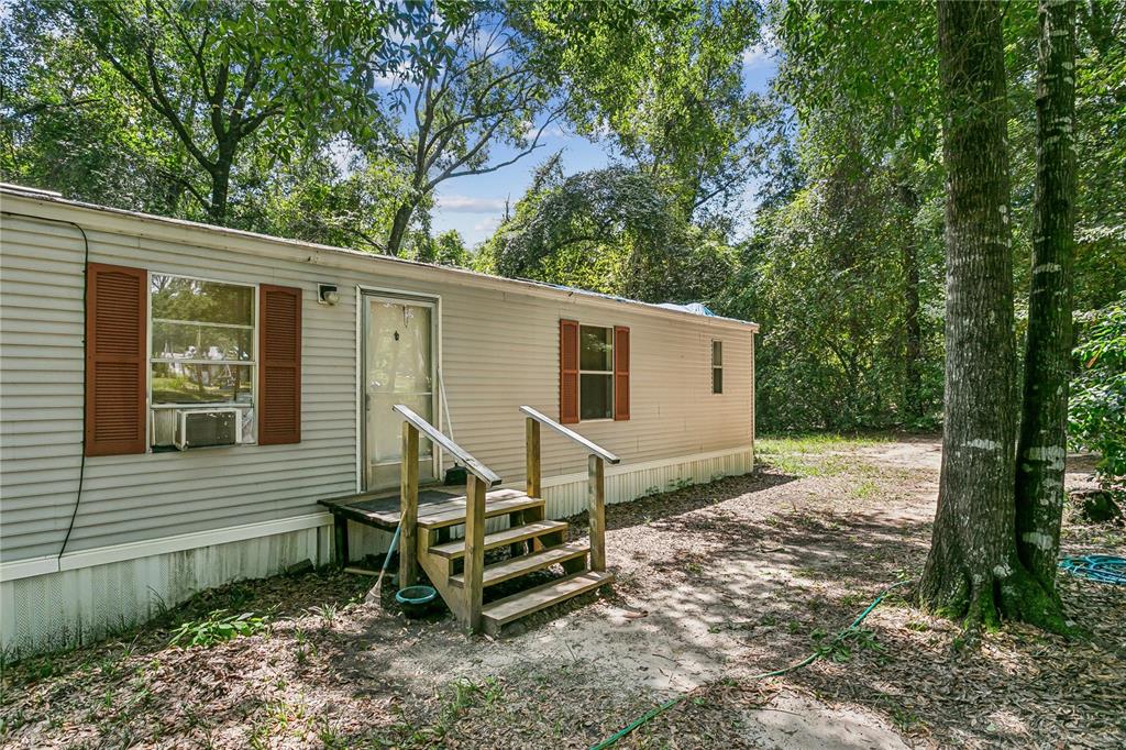 A single-story mobile home with tan siding, brown shutters, and wooden stairs in a wooded area — 2323 CAMORS ROAD, JAY, FL