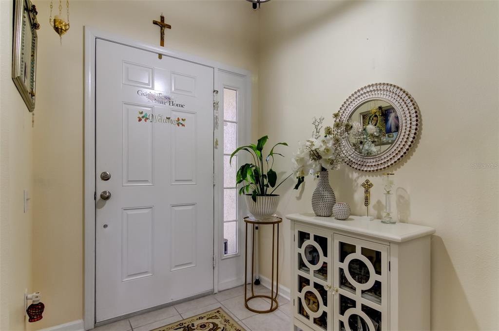 An entryway features a white front door, a patterned console table, and a round mirror — 26642 CASTLEVIEW WAY, WESLEY CHAPEL, FL