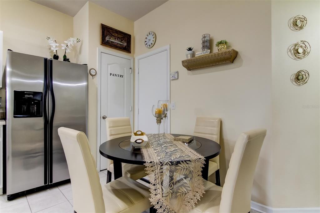 A dining area features a round table with four chairs, a pantry door, and stainless refrigerator — 26642 CASTLEVIEW WAY, WESLEY CHAPEL, FL