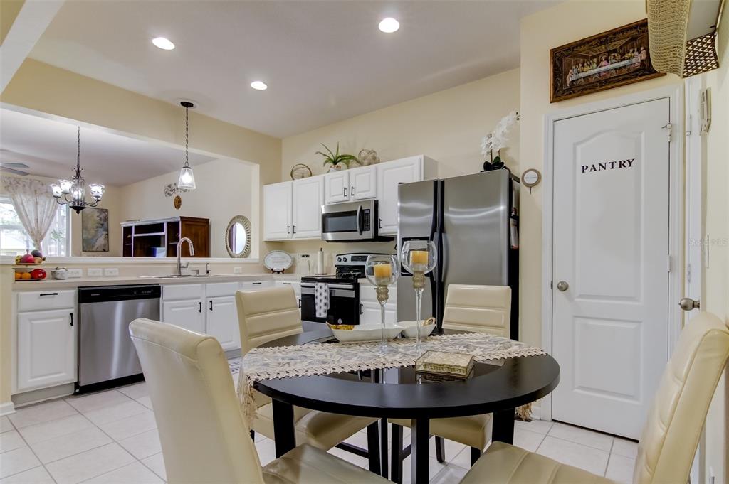 A kitchen features white cabinets, stainless steel appliances, a pantry door, and a dining table — 26642 CASTLEVIEW WAY, WESLEY CHAPEL, FL