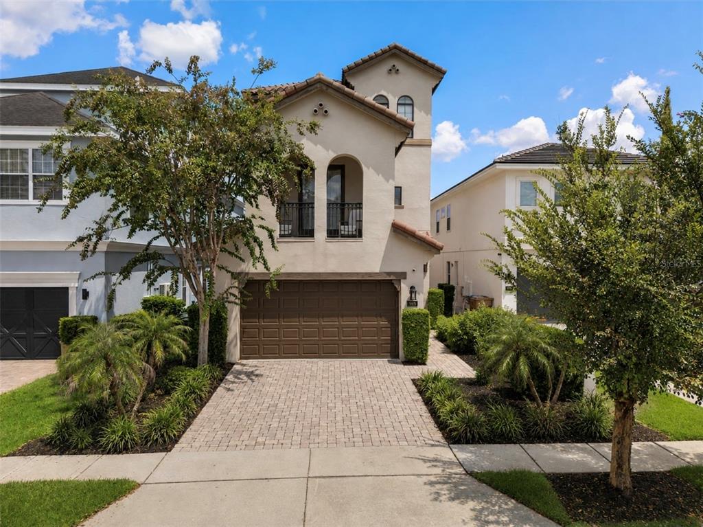A two-story stucco house with a brown garage door and arched windows under a blue sky — 969 DESERT MOUNTAIN COURT, KISSIMMEE, FL