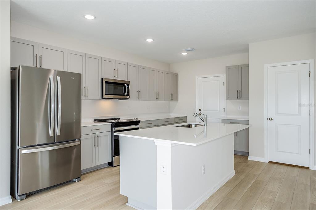 A modern kitchen features gray cabinets, stainless steel appliances, white countertops, and a central island — 34634 SILENT PINE RUN, DADE CITY, FL