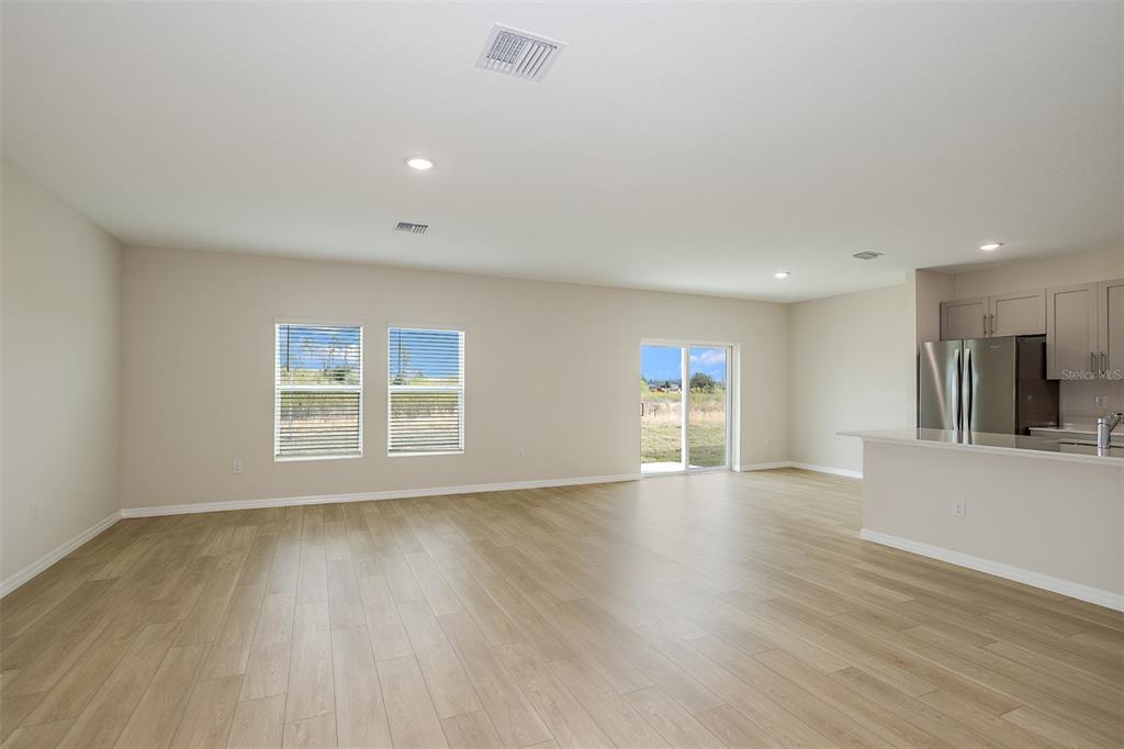 An open-concept living area features light wood-look flooring, neutral walls, and a kitchen island — 34634 SILENT PINE RUN, DADE CITY, FL