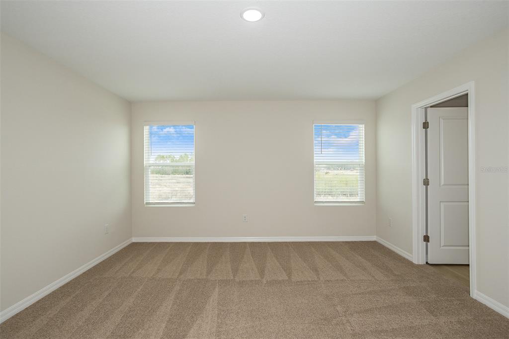 An empty bedroom features beige walls, tan carpeting, two windows, and a white interior door — 34634 SILENT PINE RUN, DADE CITY, FL
