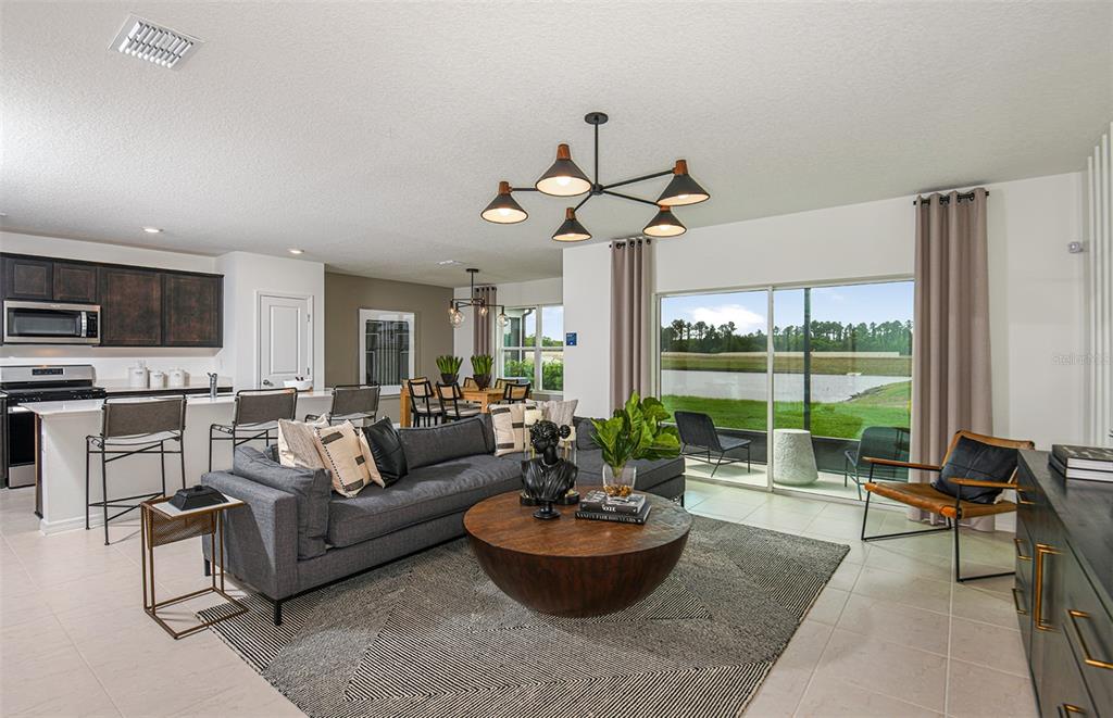 An open-concept living room and kitchen featuring a gray sectional, round coffee table, and patio — 9911 TRELLIS VINE WAY, PARRISH, FL
