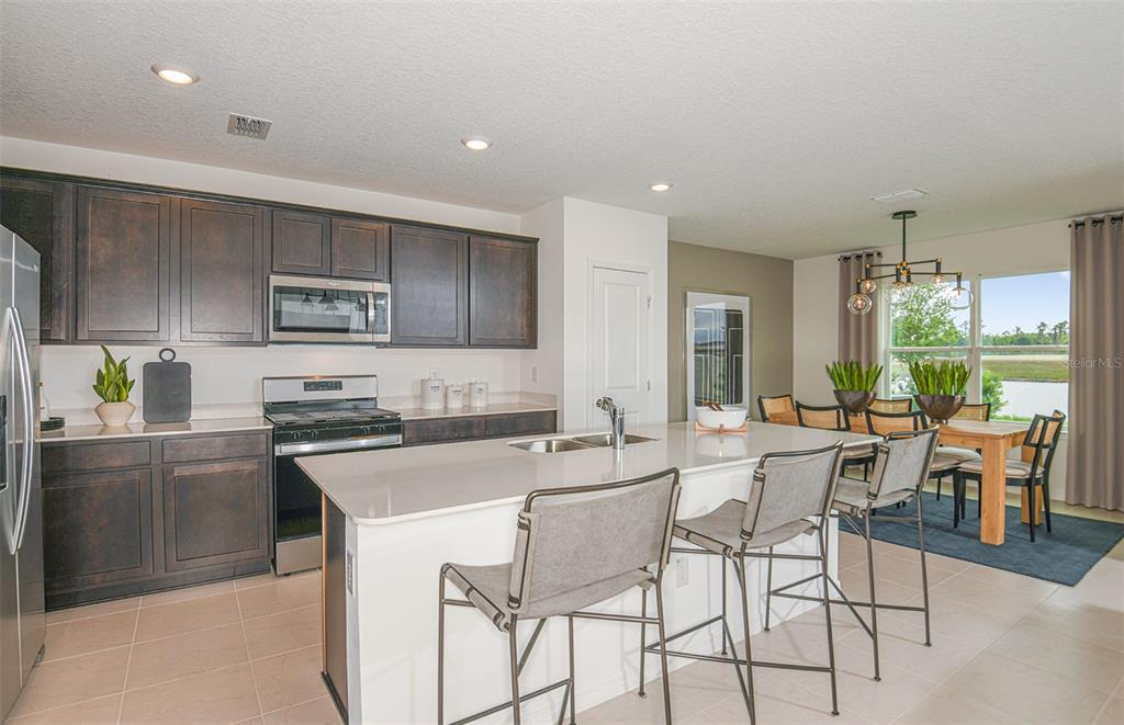 A kitchen with dark wood cabinets, a white island, and an adjacent dining area — 9911 TRELLIS VINE WAY, PARRISH, FL