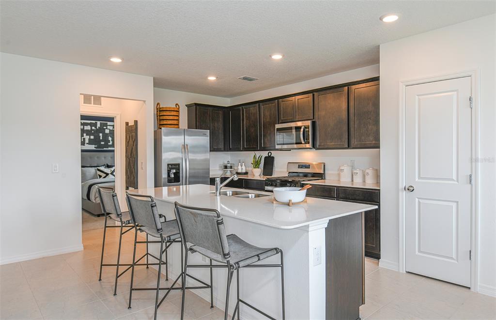 A kitchen features dark wood cabinets, a white quartz island with bar stools, and appliances — 9911 TRELLIS VINE WAY, PARRISH, FL