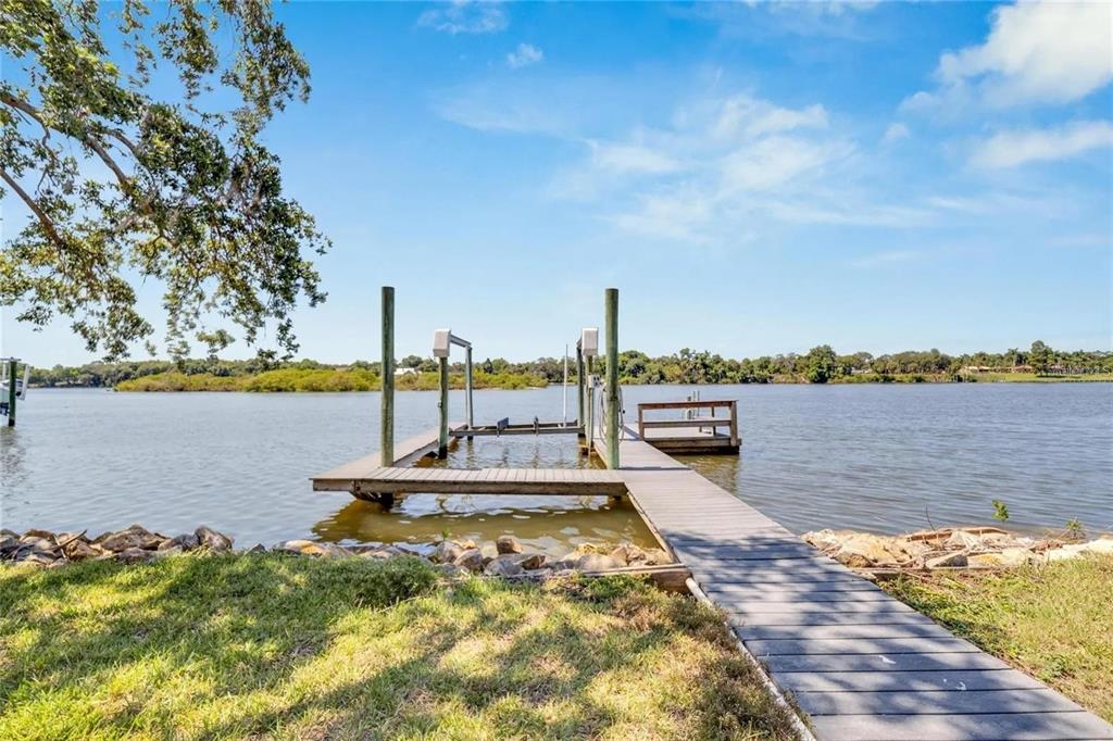 A wooden dock with a boat lift extends into a calm lake from a grassy shore — 9307 RIVER COVE DRIVE, RIVERVIEW, FL