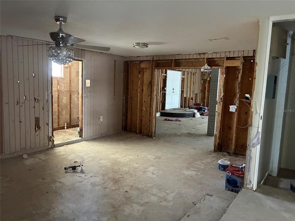 An unfinished room with exposed wall studs, concrete flooring, and a crystal ceiling fan — 9307 RIVER COVE DRIVE, RIVERVIEW, FL