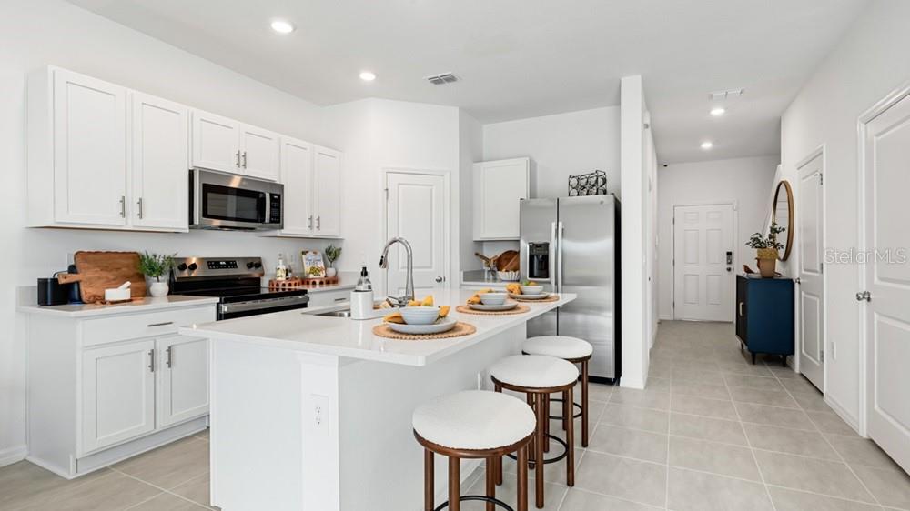 A modern kitchen features white cabinets, stainless steel appliances, a center island, and bar stools — 13203 STABLE PLACE, PARRISH, FL