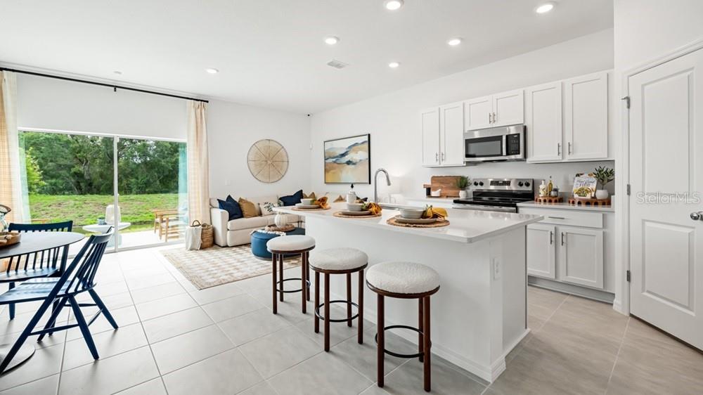 A bright open-concept kitchen and living area featuring white cabinetry, a breakfast island, and patio doors — 13203 STABLE PLACE, PARRISH, FL