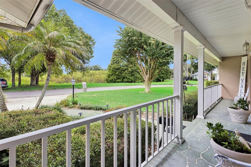 A covered porch with white railings overlooks a green lawn and trees — 5016 RIVER LAKE ROAD, WINTER HAVEN, FL