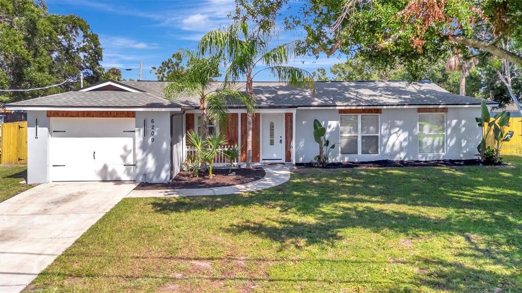 A single-story house with a white garage, wood-paneled entryway, and a palm tree in front — 6209 FLAMINGO DRIVE, APOLLO BEACH, FL