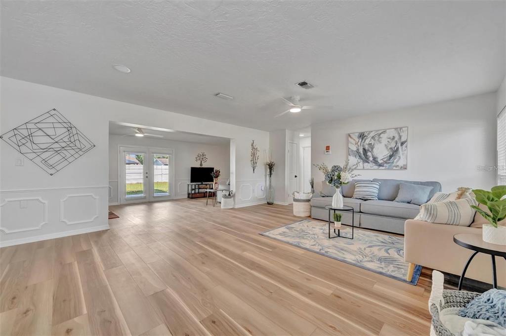A bright living room features light wood-look flooring, white walls with wainscoting, and a sofa — 6209 FLAMINGO DRIVE, APOLLO BEACH, FL