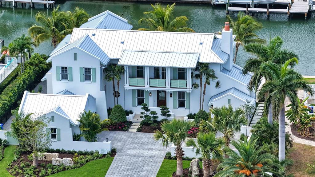 A white two-story house with green garage doors and a paved driveway under a blue sky — 711 OLD COMPASS ROAD, LONGBOAT KEY, FL