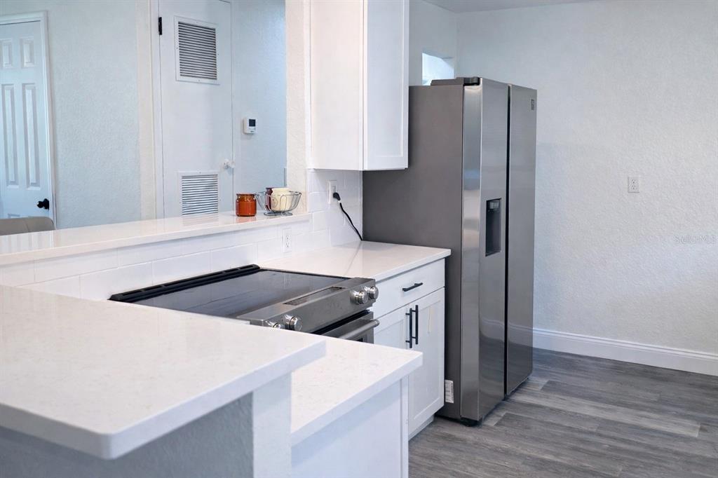 A kitchen features white cabinets, quartz countertops, stainless steel appliances, and gray wood-look flooring — 713 THOMAS AVENUE, COCOA, FL