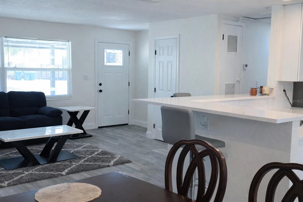 An open-concept living room and kitchen area featuring white cabinets, a breakfast bar, and flooring — 713 THOMAS AVENUE, COCOA, FL