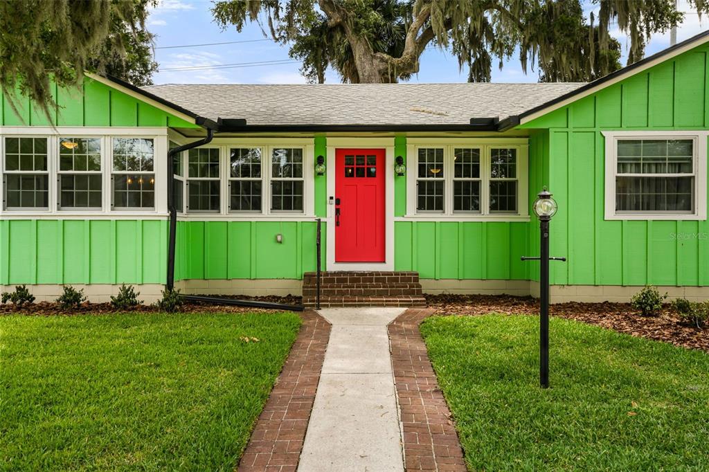 A single-story house with bright green vertical siding, a red front door, and brick steps — 1338 HEIM ROAD, MOUNT DORA, FL