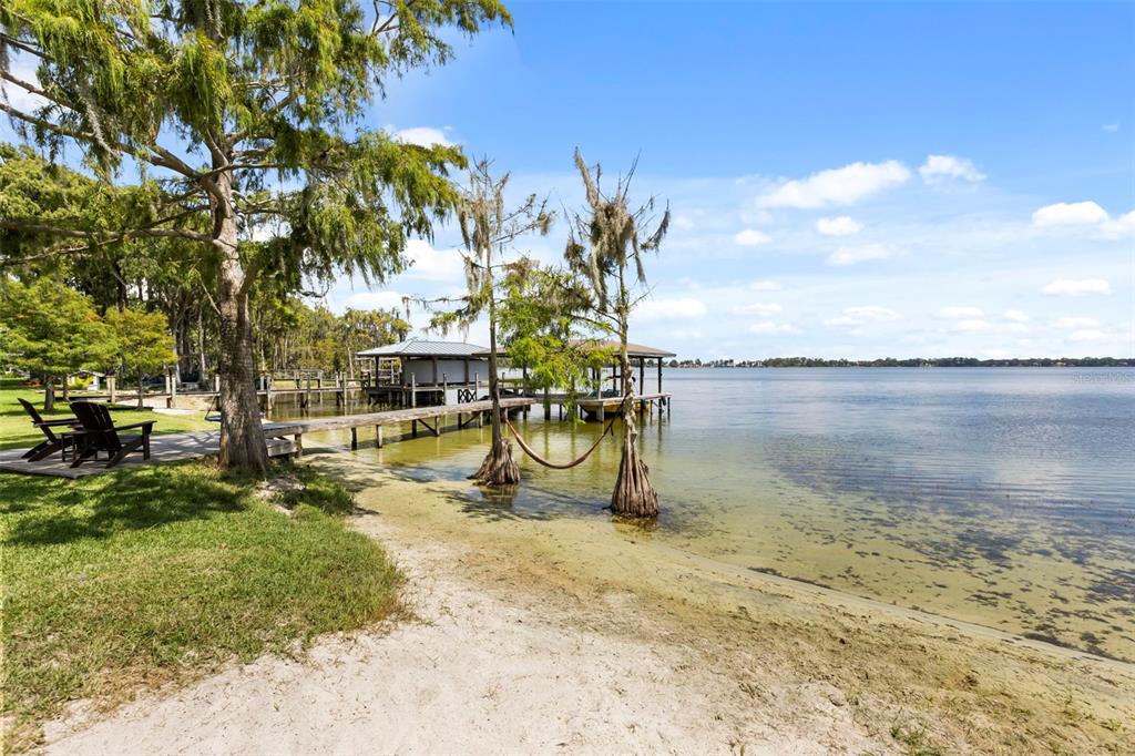 A sandy lakeshore features a wooden dock, a boat slip, and a hammock between trees — 10430 LAKE COTTAGE LANE, ORLANDO, FL
