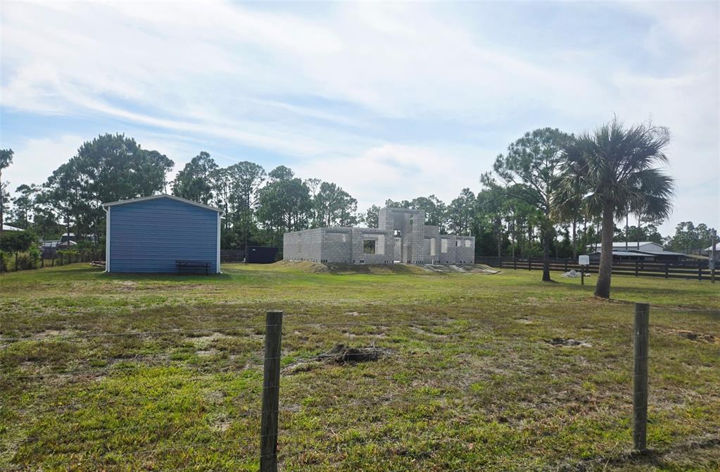 A blue shed stands next to a house under construction on a grassy, fenced lot — 7441 STRASSE BOULEVARD, PUNTA GORDA, FL