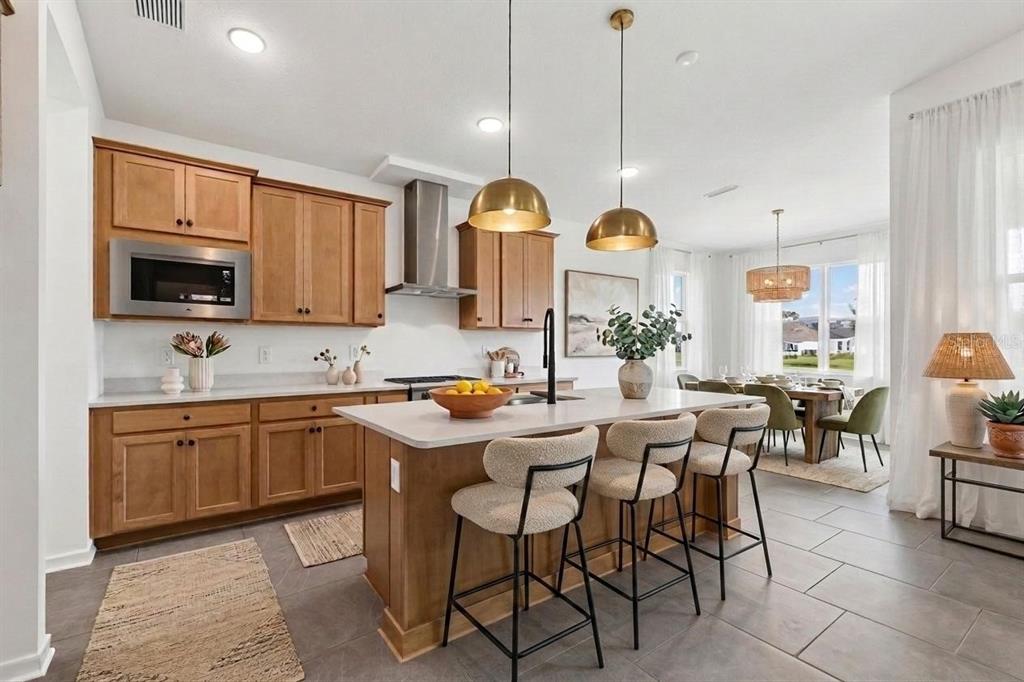 A kitchen features light wood cabinets, a central island with bar stools, and dining area — 11837 MOONSAIL DRIVE, PARRISH, FL