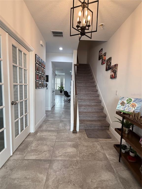 A tiled entryway features a staircase with carpeted steps, a chandelier, and a gallery wall — 8386 IRON MOUNTAIN TRAIL, WINDERMERE, FL